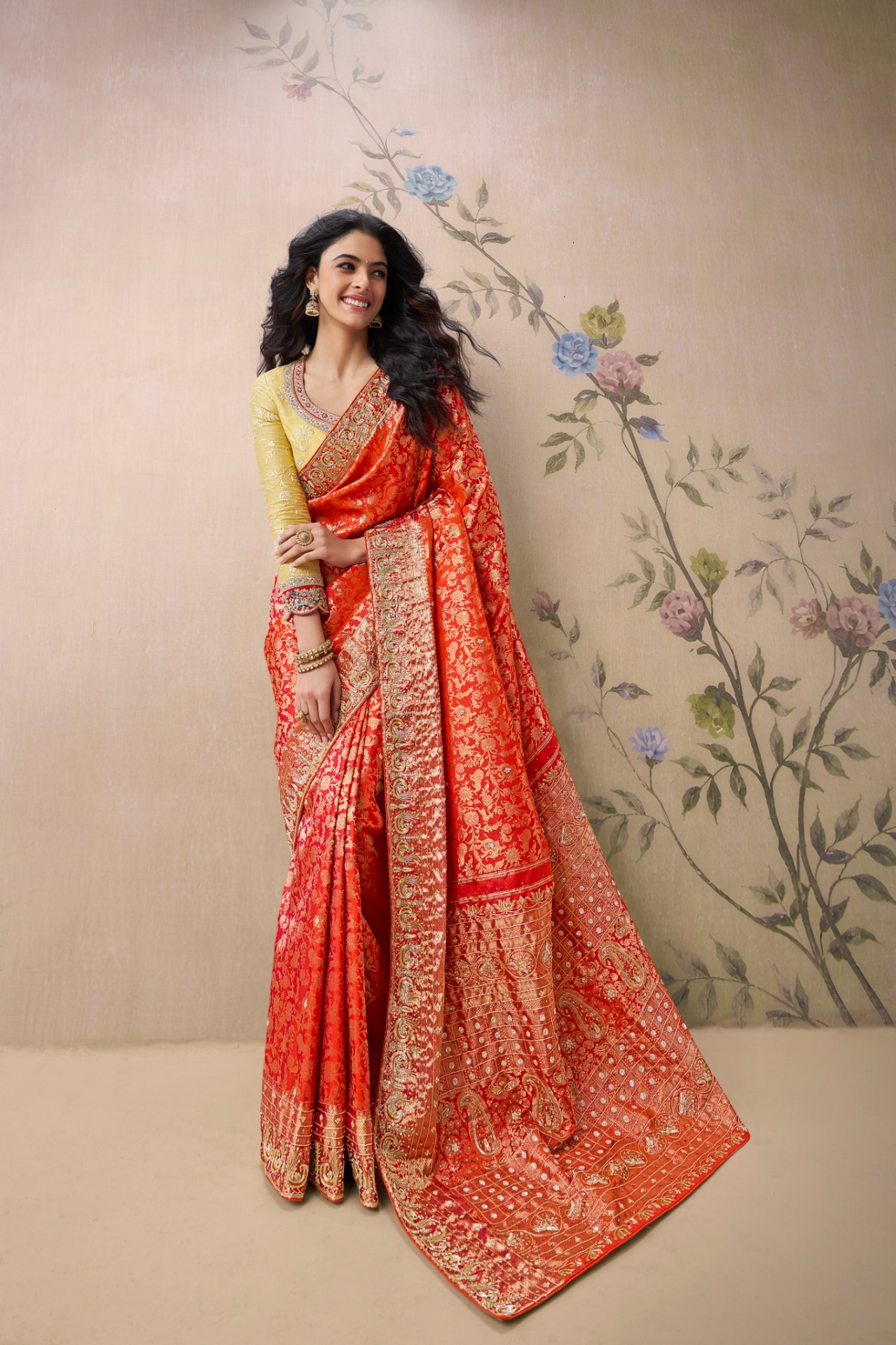 A model in a modern butterfly drape of a red Banarasi saree, with pleated pallu and statement earrings
