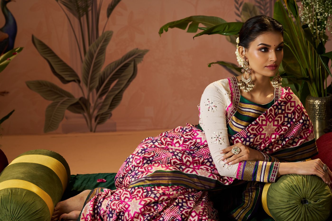Wide courtyard frame of a rose pink Bandhani saree with brass vessels and banana leaf in the set